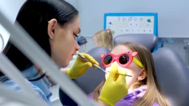 Pediatrik dişçi kız doktordan korkuyor. Doktor, dişçi muayenesi için ikna etmeye çalışıyor. Koltuk başı dişçisi, sarı lateks eldiven, kız eşofmanı.