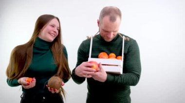 comic photo different size of breasts one breast is larger than the other is smaller girl holding fruit tangerine and cocoas smiling man next to a basket in form of box looks at teenage joke instead