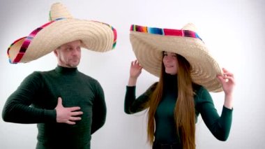 Meksika sombrero şapkalı beyaz arka plandaki adam ve kadın Napolyon gibi giyinmiş büyük bir şapkayı işaret ediyor sanki rahatlamak için denizin sıcaklığını bekleyen sıcak süveterler sunuyormuş gibi.