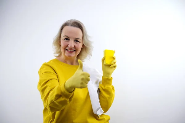 House cleaning cleaning company woman showing thumb up in yellow gloves in other hand she has sponge for washing dishes and windows of walls on shoulder white waffle towel advertising call to house