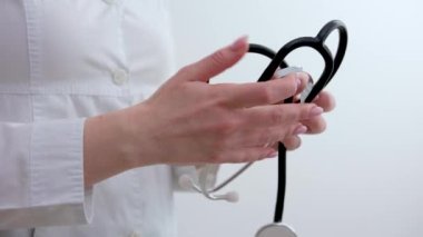 Beyaz arka planda steteskop, üst manzara. Kadın doktorun elleri fonendoskop katlıyor ve omzuna yaslanıyor.