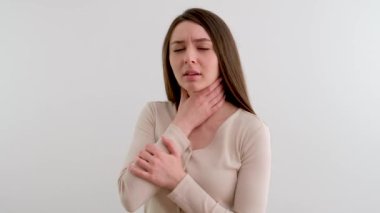 Yutması zor genç bir kadın. Boğazı ağrıyan, boğazı ağrıyan, elini boğazına dayayan bir kız. Stüdyoda, hastalığın nahoş duyguları arasında beyaz bir arka planda saklanıyor.