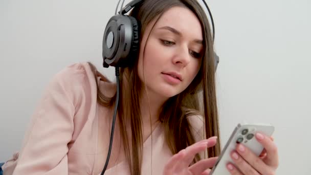 彼女の手に携帯電話を持つ若い女の子はクラスのチケットテストにインターネットの答えに試験の外観を渡すために自宅でオンライン学習のヒントで音楽の仕事に耳を傾けメッセージを入力しています — ストック動画