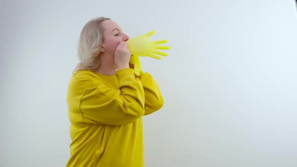 一只手拿着一只白色背景的膨胀的黄手套 一个穿着鲜艳的黄衣服的女人把一只手套吹起来 比喻诈骗 欺骗清洁医生的笑话 — 图库视频影像