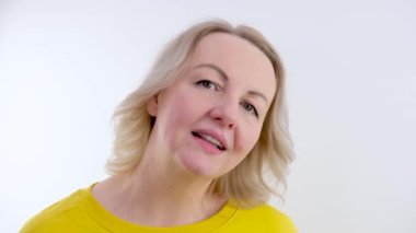 Sarı elbiseli kadın rahatlamış görünüyor omuz silkiyor beyaz arka planda gülümseyen sarışın hoş bir kadın.