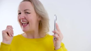 Telefonun elinde dans eden bir kadın seviniyor. Telefona bakıyor. İyi haberler, sarı elbiseler, beyaz arka plan.