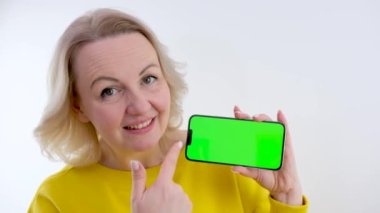 Telefonu olan güzel bir kadın. Yeşil arka plan krom anahtarı. Gülümseyen bir parmak.