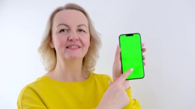 Telefonu olan güzel bir kadın. Yeşil arka plan krom anahtarı. Gülümseyen bir parmak.