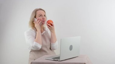 Yetişkin bir kadın kırmızı elmayı beyaz arka planda ısırmaktan mutluluk duyar. Masa başı diyet yemek tarifleri, internet üzerinden beslenme önlüğü ve beslenme programları.