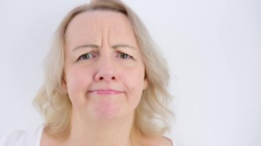 Photo of thoughtful woman bites lower lip, looks with dreamy expression aside, wearing stylish beige hoodie, stands against white wall. Copy space for your text. High quality photo