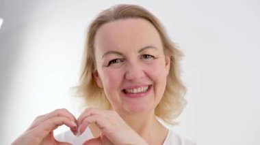woman sincerely smiles with hands shows a heart squinting her eyes on a white background love feelings joy valentines day like goods product delivery advertising space we I love it love you