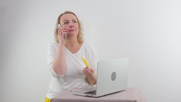 白い背景の中年女性は立っている横にノートパソコンの手でテーブルの近くに彼女の唇を保持笑みを浮かべてフレームに見えます — ストック動画