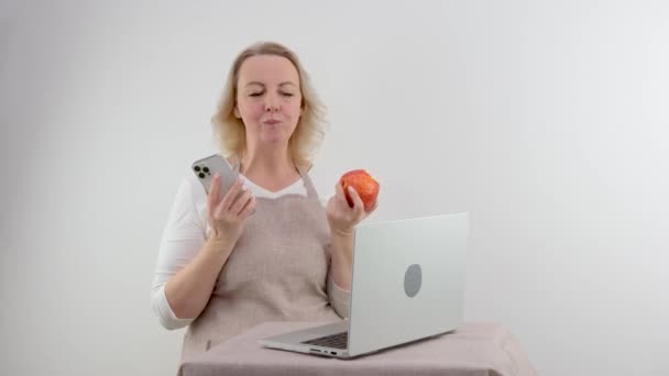 4月の携帯電話のラップトップ自宅の階段に座ってリンゴを食べながら 彼女のスマートフォンを使用して美しい女性のショット 高品質の写真 — ストック動画
