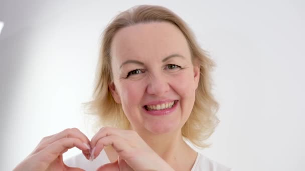 Woman Sincerely Smiles Hands Shows Heart Squinting Her Eyes White — Stockvideo