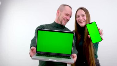 Bu yeni uygulamayı kullan. Neşeli çift akıllı telefonu ve dizüstü bilgisayarı boş ekranla gösterir, mobil uygulamayı tavsiye eder, web sitenizi tanıtır, tasarım için modelleme yapar. Krom anahtar yeşil ekran seçici odak