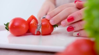 Çocuğa yakın çekim. Domatesçi çocuk ya da kız, annelerinin yanında peynir bıçağıyla sebze kesmeyi öğreniyor. Beyaz porselen yemek pişirmeyi öğreniyor.