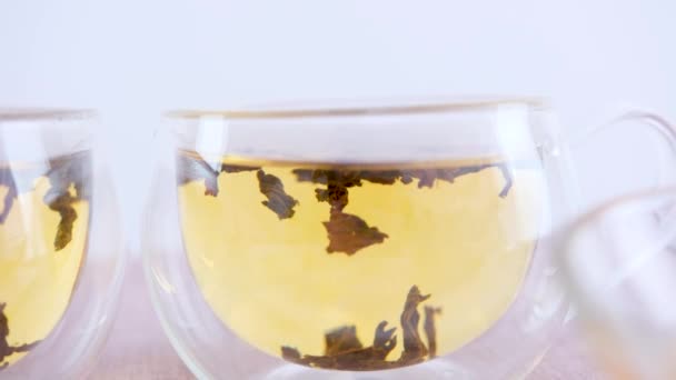 お湯で渦巻く大きな葉のガラスの中ですぐに黒茶の二重底のコップが醸造されます — ストック動画