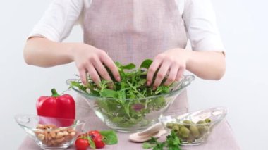 girl mixes lettuce with hands she pours it into glass plate vegetarian food healthy food wooden spoons apron tablecloth young woman teenager prepares dinner for family dinner breakfast lunch