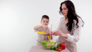 Mutfakta Anne ve Şirin Küçük Çocuk Sağlıklı Yemek Yapıyor. Ebeveynler küçük oğluna sağlıklı alışkanlıkları ve sebzeleri salata kasesinde nasıl karıştıracağını öğretiyor. Sevimli Çocuk Ailesine Yardım Ediyor
