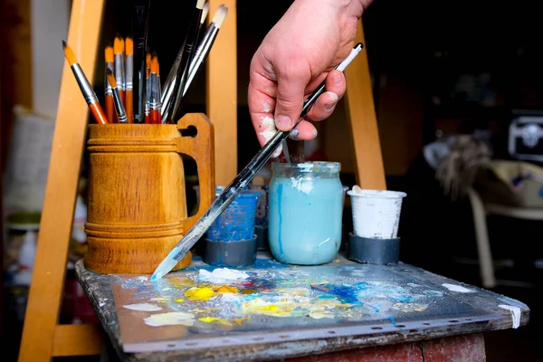 artist paints a picture of oil paint brush in hand with palette closeup. High quality photo