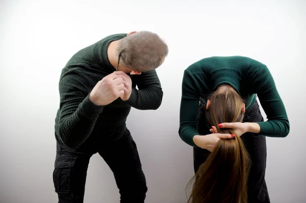 girl straightens her hair while doing her hair a man teases her in men a thin pigtail on the back of his head he leans over pulling her to the side having fun laughing Prank white background
