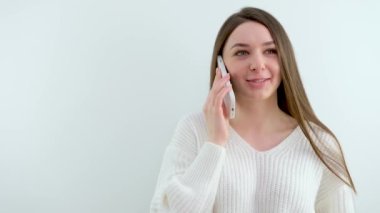 Çekici genç bir kadın telefonda konuşuyor. Gri arka planda tek başına duruyor. Yüksek kalite 4k görüntü
