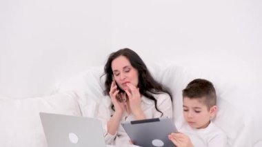 Serbest çalışan anne ev hapsi sırasında kanepede oturur. Uzaktan kumandalı bilgisayarda çalışır. Çocuk tablet kullanıyor, tablette oyun oynuyor, annesiyle kanepede oturuyor. Aile, tele-çalışma, e-öğrenme