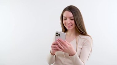 Düşünen genç, sarışın bir iş kadını, atölyedeki gri arka planda duran akıllı telefonunu kullanıyor. Yüksek kalite 4k görüntü