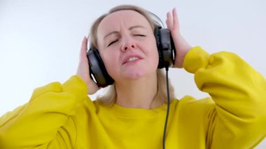 Dansçı kız kulaklıkla müzik dinliyor, şarkıdan hoşlanıyor. Mavi arka plan 4K 'de sarı kazaklı komik kız fotoğrafı. Yüksek kalite 4k görüntü