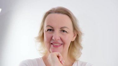 Mutlu 40 'lı yaşlarda olgun bir kadın yüz derisine dokunuyor kameraya bakıyor aynada pohpohluyor eski sağlıklı kuru cilt bakımı güzellik konsepti cilt bakımı, kozmetik ve yaş karşıtı estetik cerrahi.