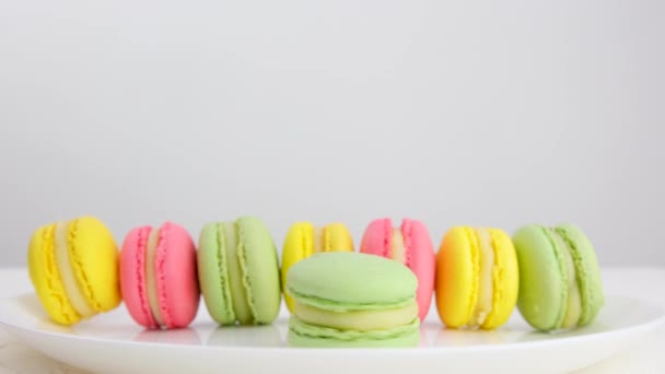 Много Разноцветных Французских Макаронных Десертов Стоят Тарелке Белом Фоне Рука — стоковое видео