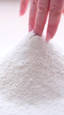 pile of white wheat flour was poured on Light Table womans hand with French manicure destroys structure she prepares places for introducing eggs and notes dough for making desserts bread pizza