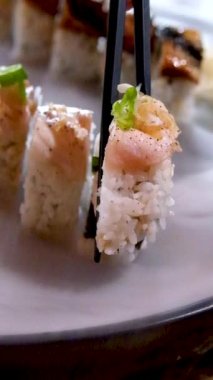 Siyah Çin yemek çubuklarının yakın plan çekimi tabaktan soğuk buz buharı ile siyah taş tabağa dökülen suşiyi alır güzel video restoranı suşi reklamı nefis Japon yemekleri servis eder.