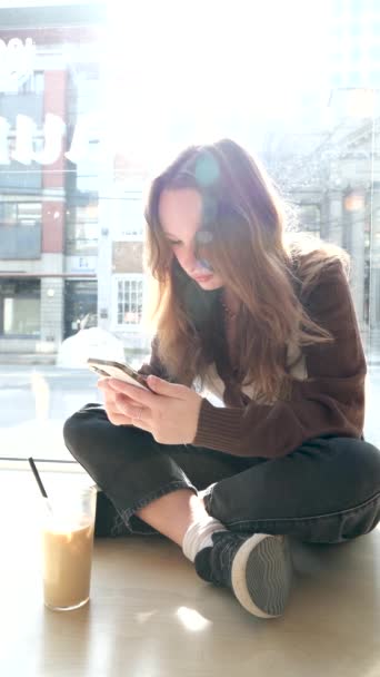 迷人的女孩喝着冰冷的咖啡 看着智能手机 一个有着伤疤的时髦少年与朋友聊天 面带微笑 在大城市的夏天 日落时的女孩高质量的照片 — 图库视频影像