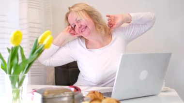 Sabahları bilgisayar başında çalışan bir kadın, monitörün yanına uzanıyor kahvaltı masasının üzerinde beyaz elbiseler, sarı duvarlar, lezzetli laleler çevrimiçi serbest çalışmak için harika bir yer.