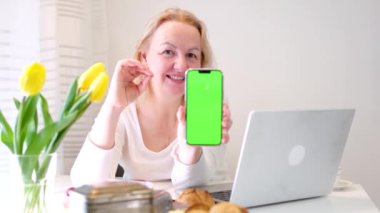 Kadın, başparmağını kaldırmış elinde hava öpücüğü, yeşil ekran krom anahtar telefon, dizüstü bilgisayarın yanında tavsiye edilen sarı laleli kahvaltı, mutlu bir kadın, size bir reklam sunuyor.