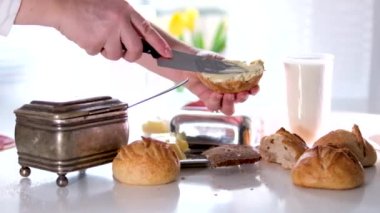 Kadın elleri bıçakla sımsıkı kavrulmuş hamur hamuru ekmeğine sürülmüş taze mayasız kahvaltı masası beyaz masa cam bardakta lezzetli hamur işleri büyük kadim şeker kasesi mutfağında süt