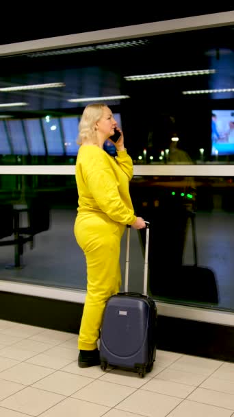 Kobieta Jasnożółtym Dresie Lotnisku Stoi Przy Oknie Walizką Rękach Rozmawia — Wideo stockowe