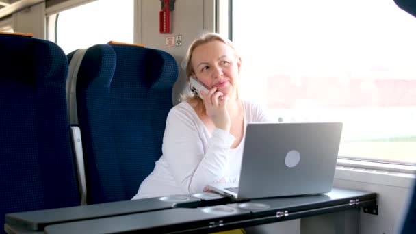 中年の大人の女性電話で話す電車の中で旅行は 近くのコンパートメント快適な椅子に便利で快適な着席車のノートパソコンの仕事レジャーの組み合わせで電話を見て置く — ストック動画
