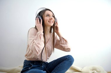 Kız yatağı başını kaldırmış kulaklıkla müzik dinliyor gülüşler dinliyor beyaz bir arka planda hoş bir hobi ediniyor. İnternet üzerinden iş konferansı için çekici kulaklıklı bir kız var.