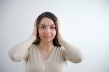 Kız şaşırır, iki elini başının üstüne koyar ellerini kaldırır ve çerçeveye bakar genç bir kadın beyaz arka planda genç ve güzel bir yüzle gençlik gülüşü