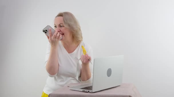 電話で話す深刻な不満女性は彼女の手はさみとメートルの減量の食事療法でノートパソコンに見えます医者と通信するのに疲れて栄養士中年白人の背景 — ストック動画
