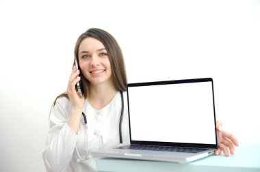 Telefondaki kadın doktor, beyaz arka planda dizüstü bilgisayarı olan bir kadın doktorun reklamını yapmak için laptopunun önündeki çağrıya beyaz ekranla cevap veriyor. Yüksek kalite fotoğraf
