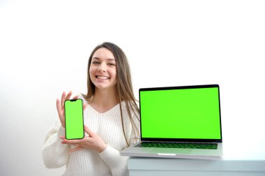 Beyaz kazaklı güzel bir kız elinde kromakey olan bir dizüstü bilgisayar gösteriyor. Bir ürünün reklamını yapıyor. Güzel bir sunum.