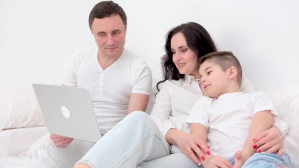 家人坐在沙发上看着笔记本电脑 工作室拍摄 家人和儿子在床上看和玩平板电脑 — 图库视频影像