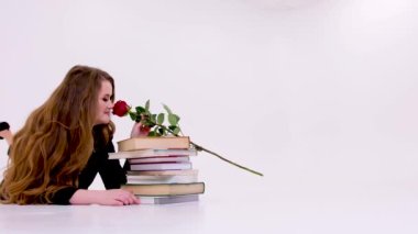 Üniversite kadın öğretmeni elinde gül, elinde yüksek topuklu ayakkabı giyen, siyah giysili seksi öğretmenle ders kitaplarının üzerine uzanır. Kırmızı gül eğitimi için beyaz saçlı, akıcı bir arka planı vardır.