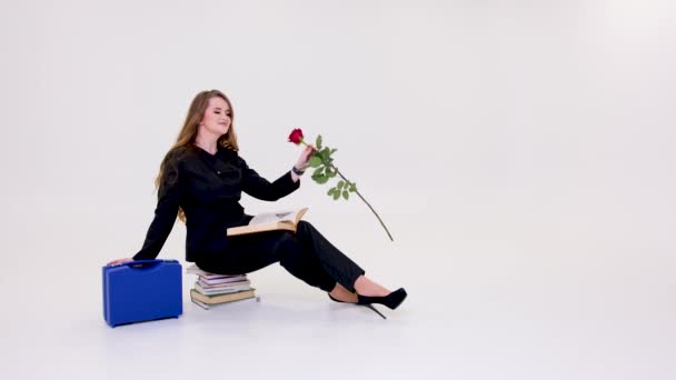 Mädchen Sitzt Auf Büchern Schnüffelnd Rote Rose Weißen Hintergrund Raum — Stockvideo