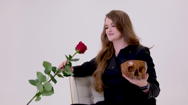 黒の女を手に持っていますA赤バラで一方でA人間の頭蓋骨Insidious女性吸血鬼ゴージャス髪オンザ白の背景失われた愛スタジオ致命的な女の子 — ストック動画