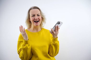 Sarı yağmurluklu güzel esmer kadın gri arka planda izole edilmiş bir cep telefonu ekranını gösteriyor. Model kablosuz kulaklık takıyor. Reklam için yer var. Yüksek kalite fotoğraf