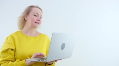 Sarı kazaklı bilişim kadını dizüstü bilgisayarda çalışıyor. Parmak işareti yapıyor. Sade pastel, açık mavi arka plan stüdyo resmi üzerinde izole edilmiş bir alanda çalışıyor..